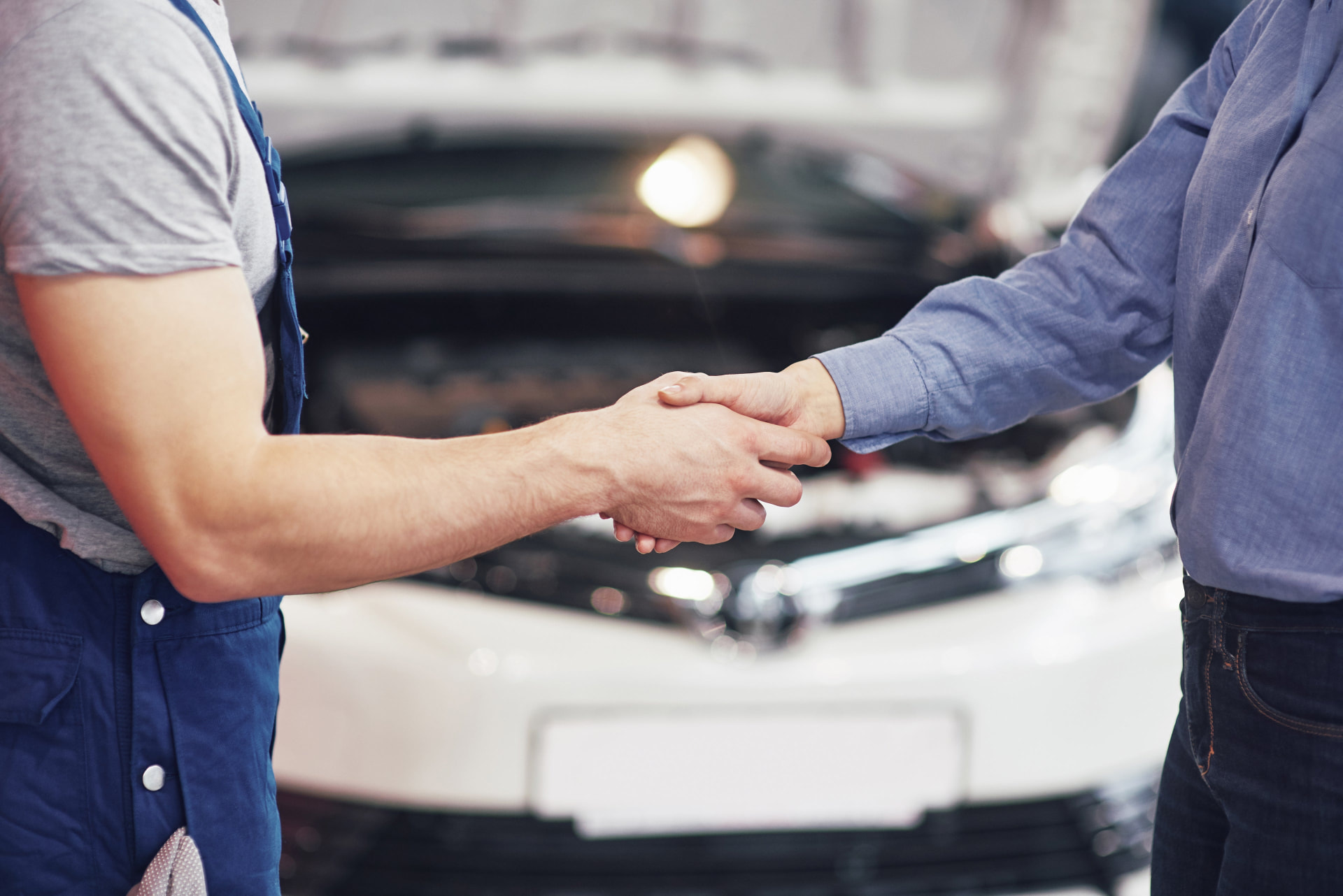 Gutachter und Kundin geben sich vor einem Fahrzeug die Hand